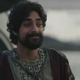 Eman Esfandi as Ezra Bridger, bearded and in robes, by a lake in Star Wars: Ahsoka.