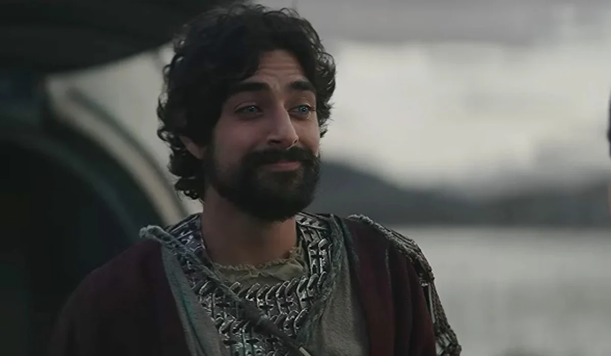 Eman Esfandi as Ezra Bridger, bearded and in robes, by a lake in Star Wars: Ahsoka.