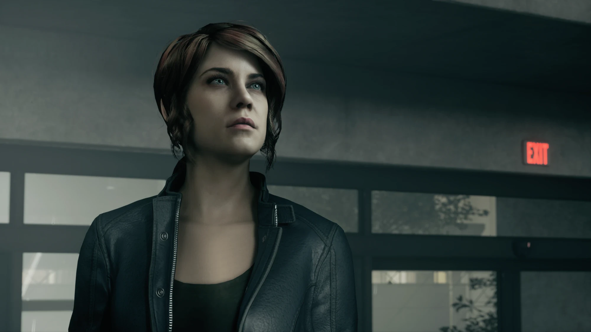 Jesse Faden, protagonist of the original Control, stands beneath a red EXIT sign.
