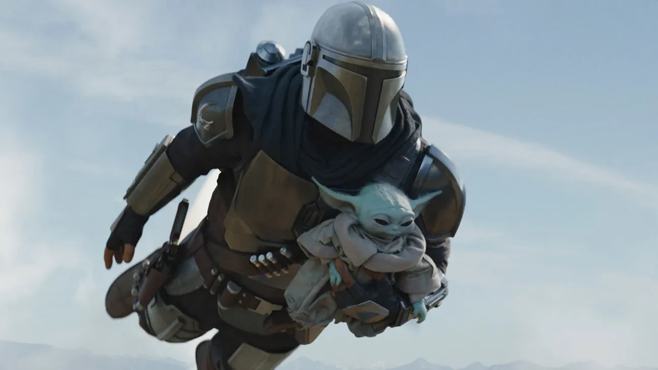 Din Djarin flies with a jetpack while carrying Grogu in The Mandalorian.