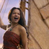 Moana, played by Catherine Laga'aia, laughs while holding a rope on her sailing canoe in Disney's live-action remake.