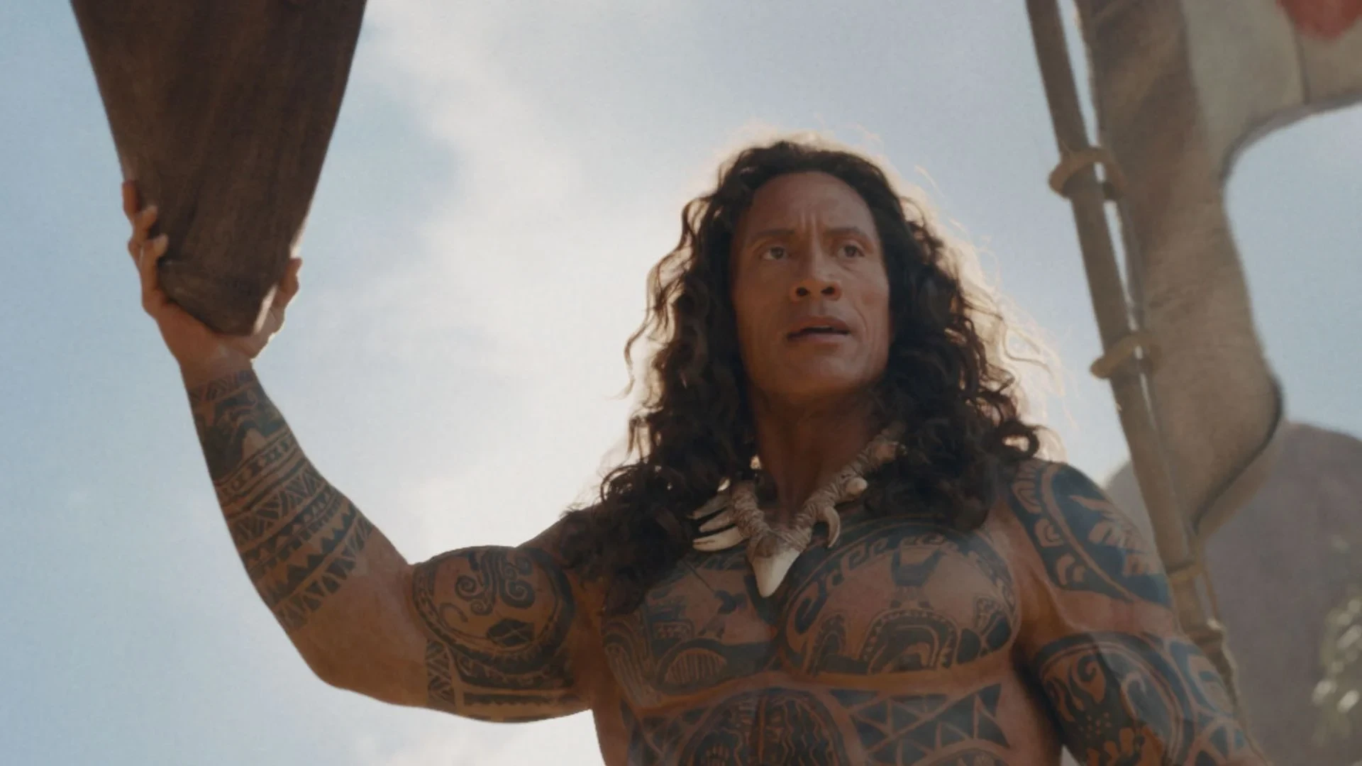 Maui, played by Dwayne Johnson, raises an oar on a canoe in Disney's live-action Moana.