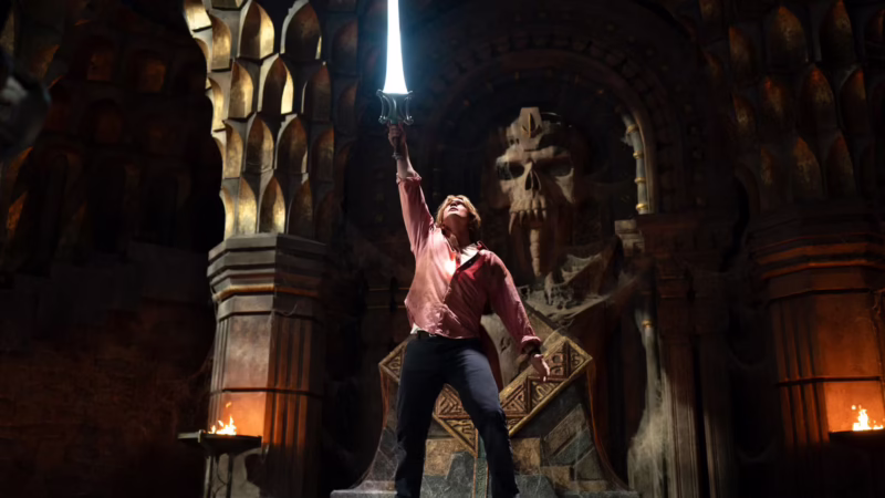 Prince Adam raises the glowing Power Sword in a torchlit throne room beneath a giant carved skull in Masters of the Universe.