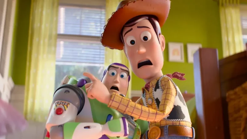 Woody points off-screen with an alarmed expression while Buzz Lightyear looks on in a child's green-walled bedroom in Toy Story 5.